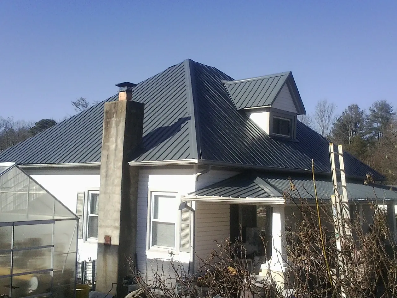 Dark blue standing seam metal roof on a white farmhouse with dormer — Slate & Tile Roof Repair by Roofing Brothers in Center Conway