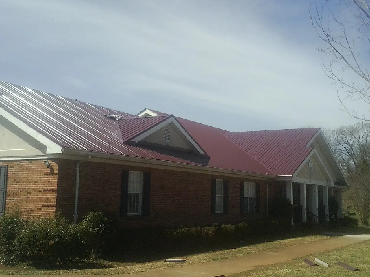 Red metal roof with gabled entries on a long brick building, from a Hail Damage Roof Repair job in Center Conway