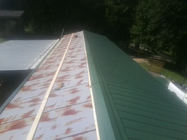 Old rusted panels beside newly installed green metal roofing — Wind Damage Roof Repair by Roofing Brothers in Center Conway