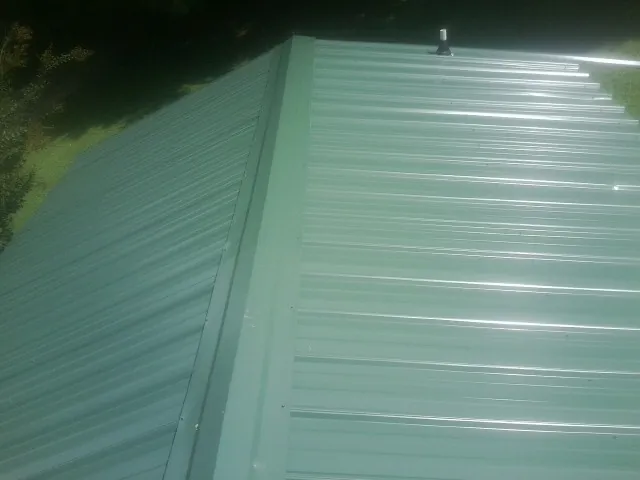 New green metal panels meeting at the ridge of a roof — Flat Roof Repair work by our crew in Center Conway