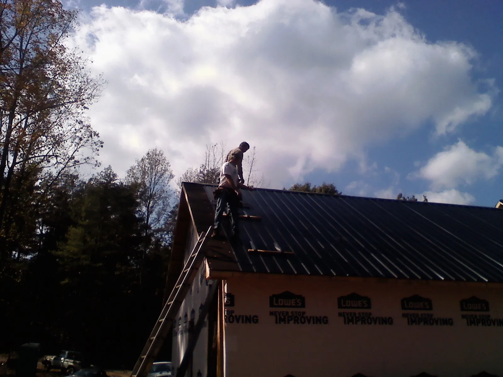 Roofer fastening dark metal panels high against a cloudy sky, from a Roof Inspection job in Center Conway
