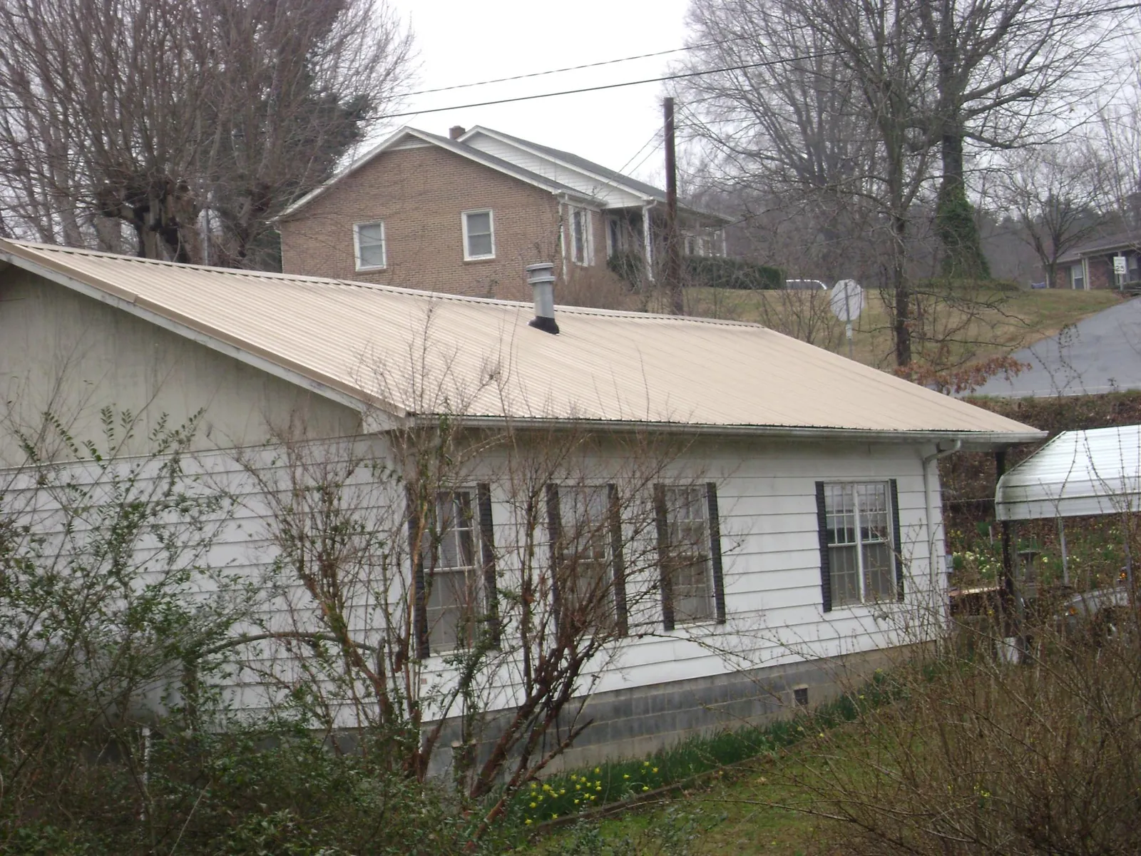 Tan metal roof on a white sided house set into a hillside — Commercial Roofing by Roofing Brothers in Center Conway